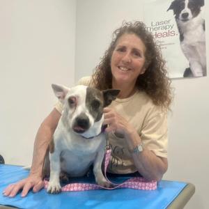 A woman is smiling and holding a small dog with white and brown fur.